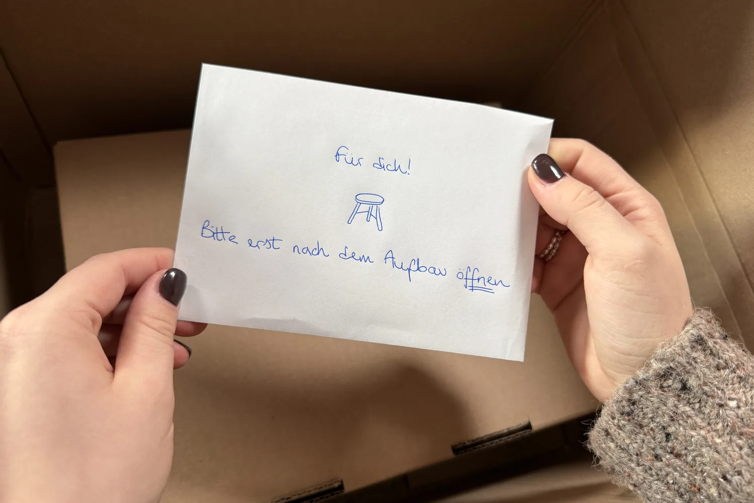 Hände halten den handgeschriebenen Umschlag „Für dich!“ über dem geöffneten Paket